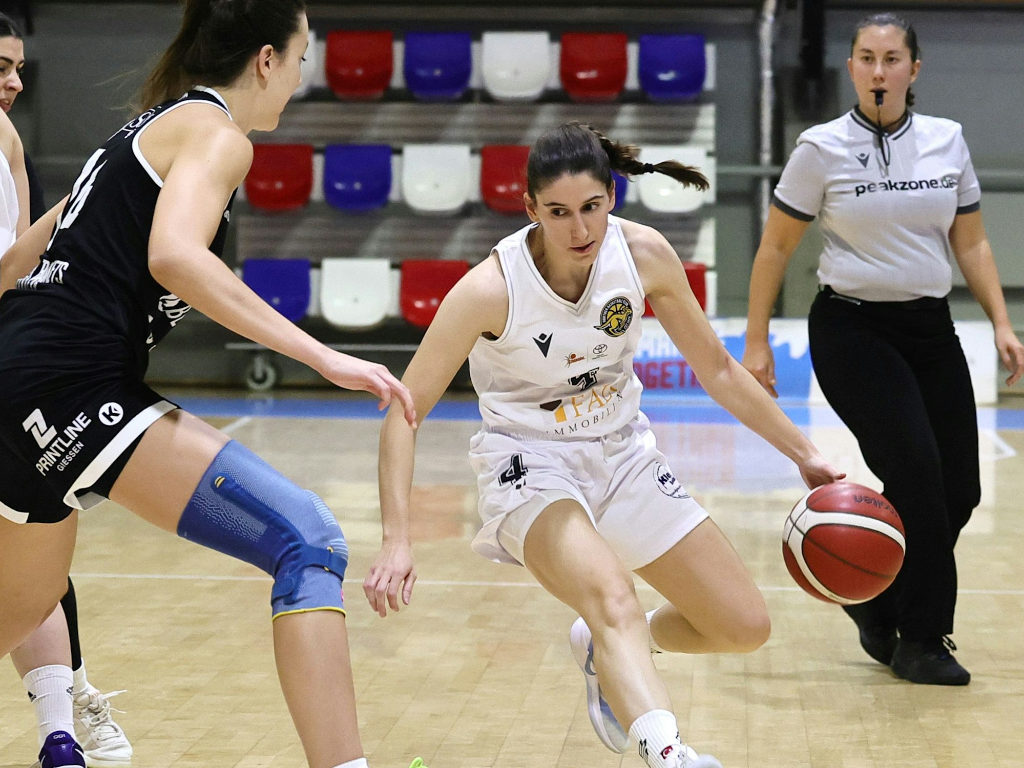 Das Foto zeigt eine Basketballspielerin des Hürther BC mit Ball, die ihre Gegenspielerin um kurven möchte.