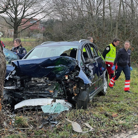 Polizeibeamte und Helfer des Rettungsdienstes an der Unfallstelle hinter dem im Frontbereich total zerstörten Fahrzeug.