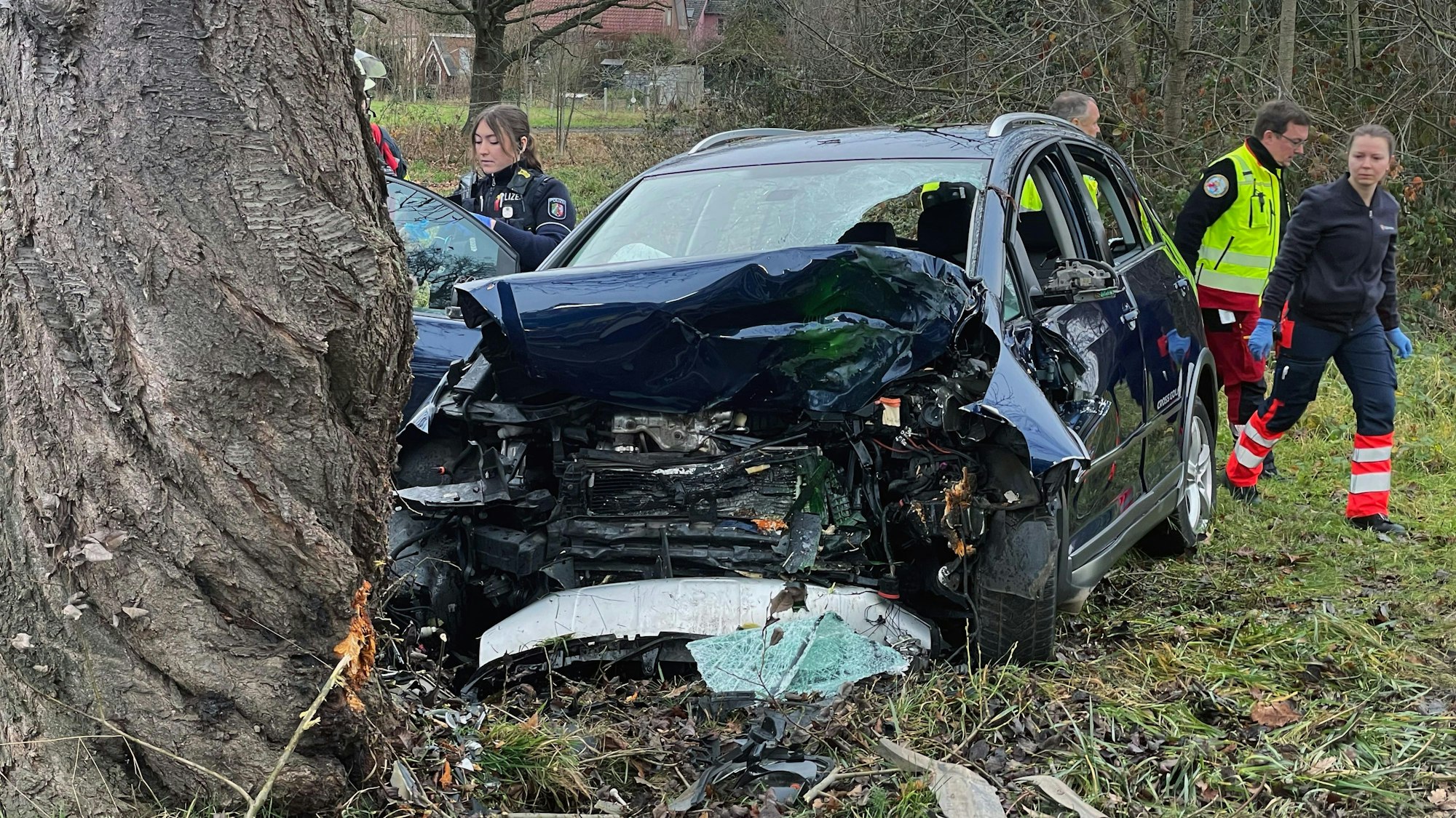Polizeibeamte und Helfer des Rettungsdienstes an der Unfallstelle hinter dem im Frontbereich total zerstörten Fahrzeug.