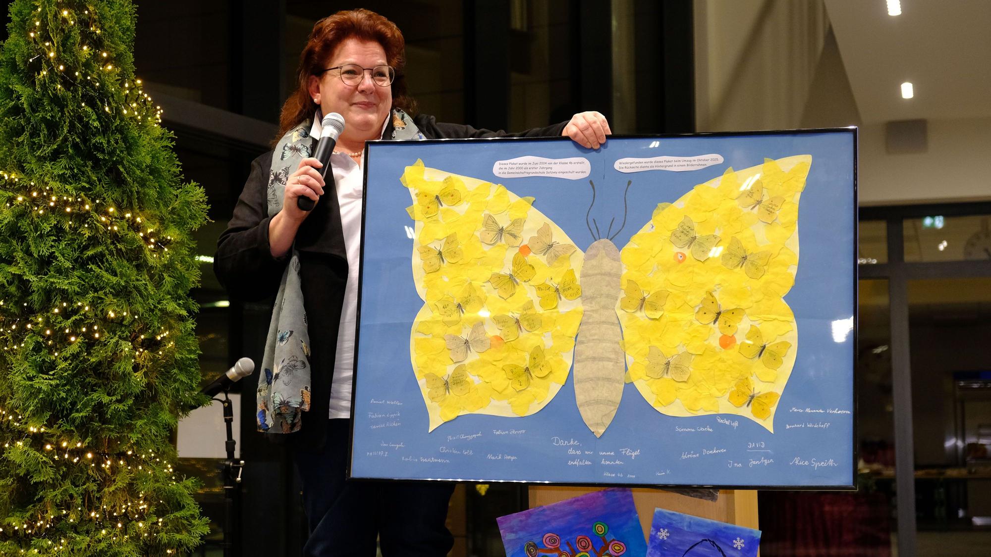 Schulleiterin Alexandra Offermann mit einem gerahmten Plakat, das einen gelben Schmetterling zeigt.