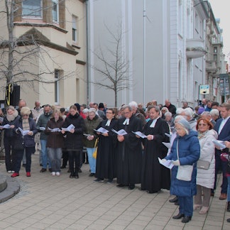 Gregor Weichsel und Michael Bork stehen am oberen Ende der Treppe vor der Kirchentür. Die Gemeidemitglieder haben Texthefte in der Hand.