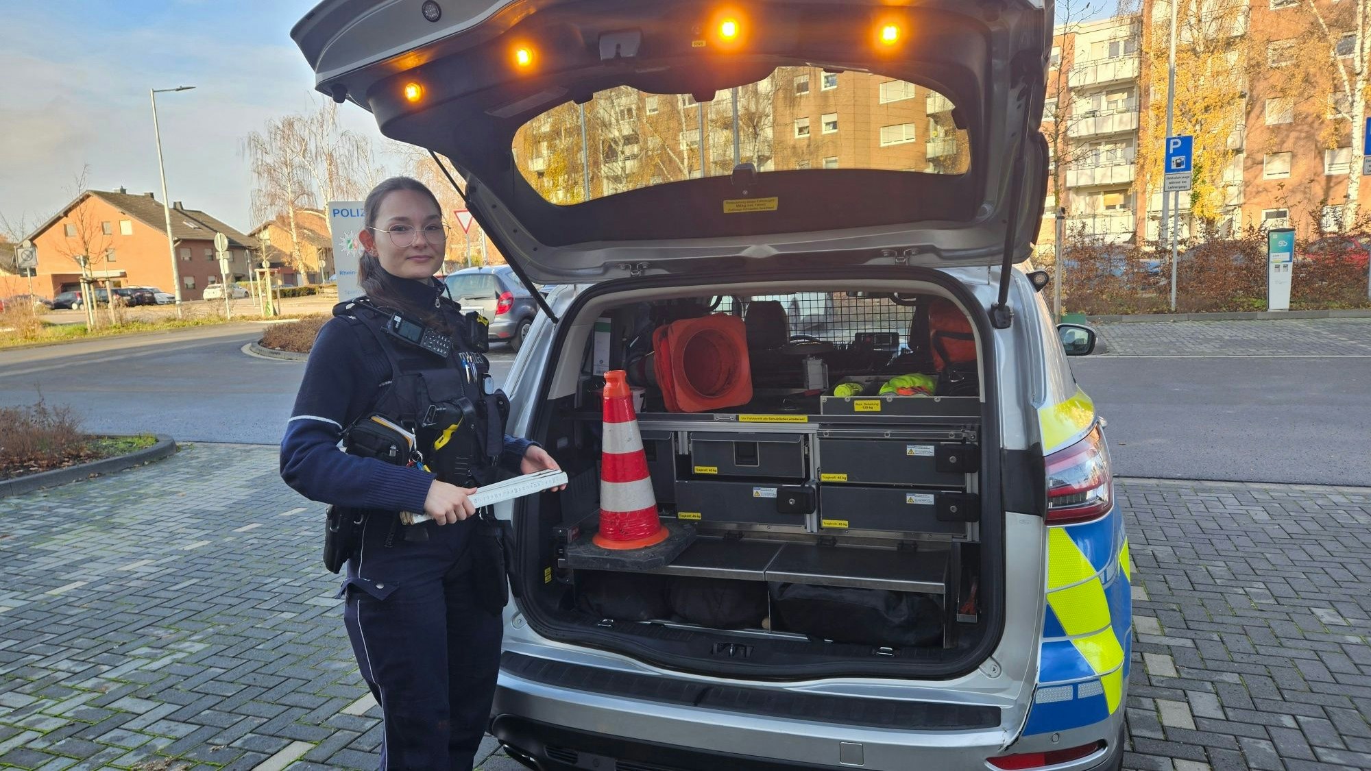 Zu sehen ist eine Polizistin an einer geöffneten Heckklappe eines Streifenwagens.