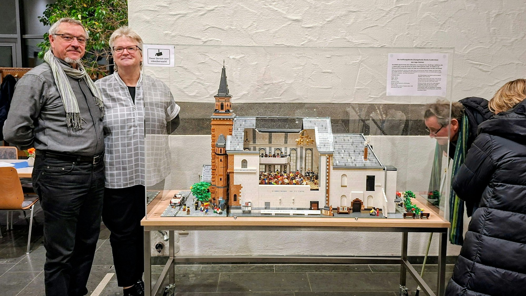 Das Modell steht hinter Plexiglas auf einem Tisch, das Ehepaar daneben. Gäste sehen sich das Objekt an.