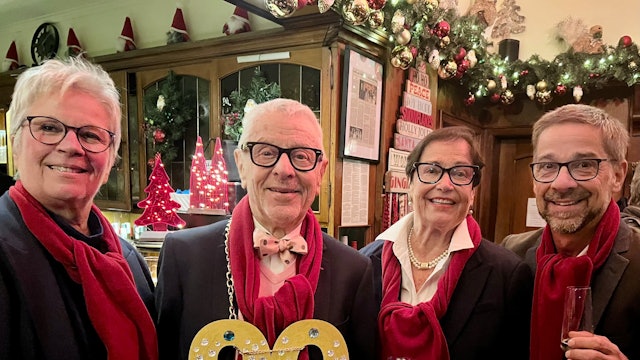 Ein Mann mit einer goldenen 90 um den Hals steht in einer Kneipe, neben ihm seine Frau und seine erwachsenen Kinder.