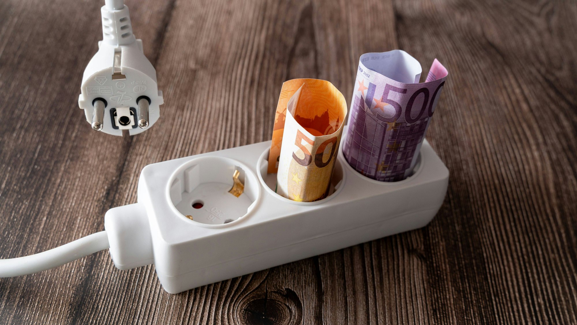 Gerollte Euro-Banknoten in Steckdosenleiste und Netzstecker