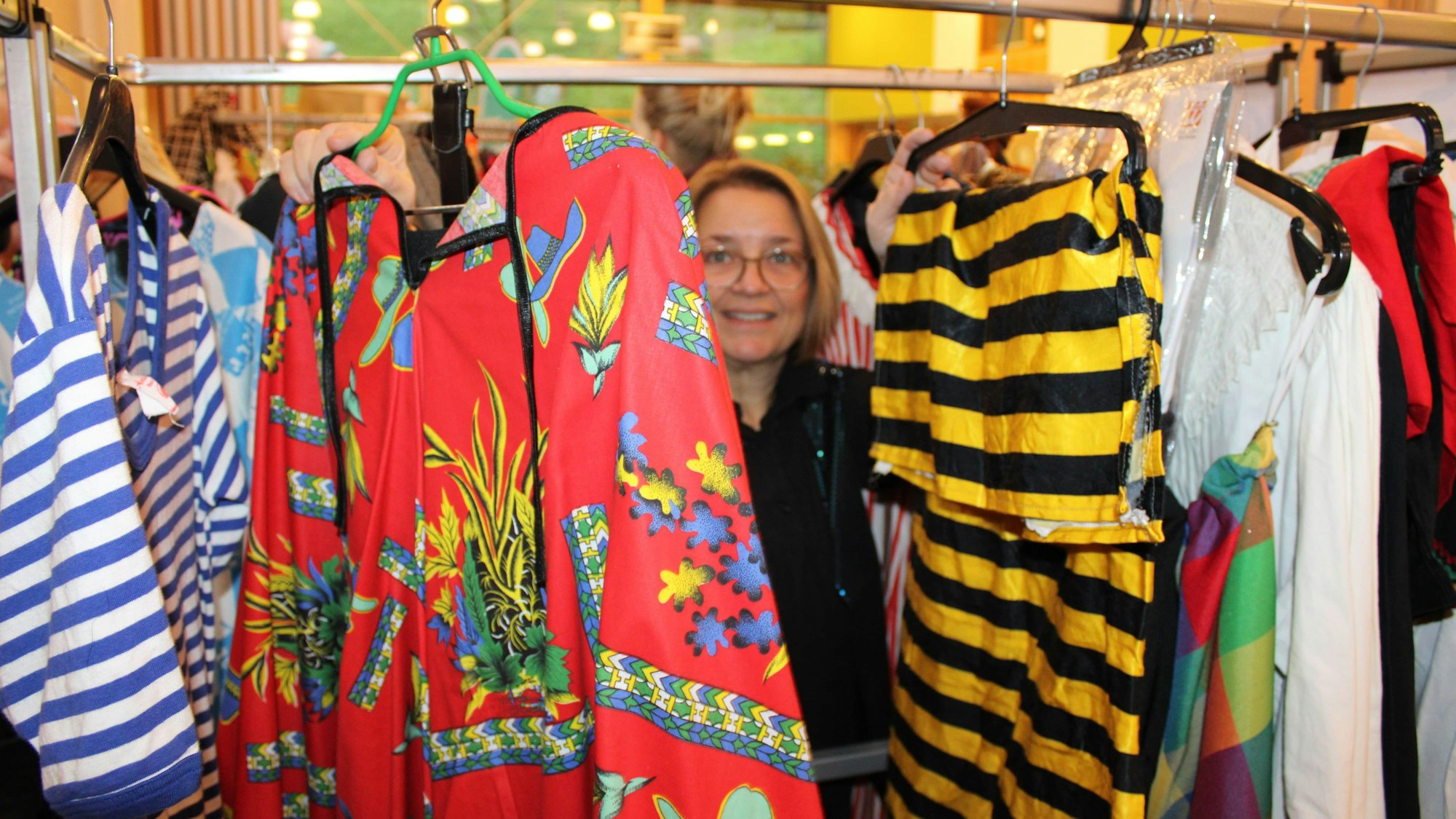 Eine Frau steht zwischen vielen bunten Kostümen.