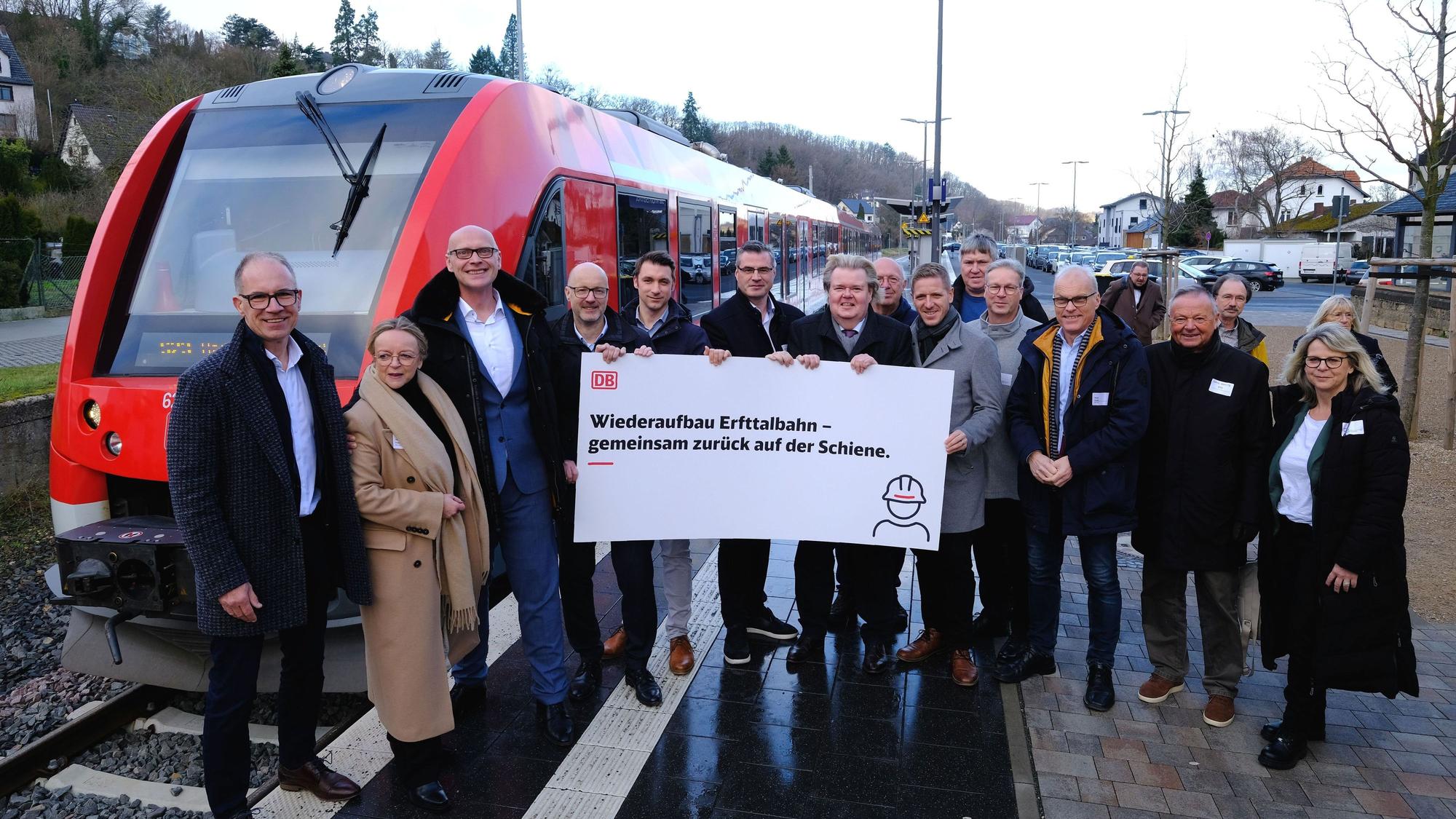 Das Foto zeigt eine Gruppe von rund 20 Personen, die mit einem Plakat vor einem Nahverkehrszug am Bahnsteig in Bad Münstereifel stehen.