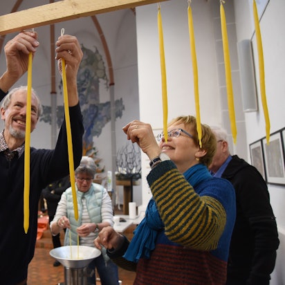 Mehrere Menschen hängen selbst gezogene Kerzen auf.