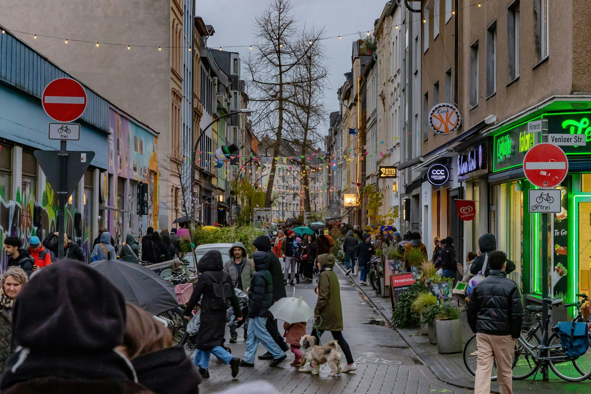 Viele Menschen mit Regenschirmen laufen in einer Seitenstraße auch auf der Fahrbahn.