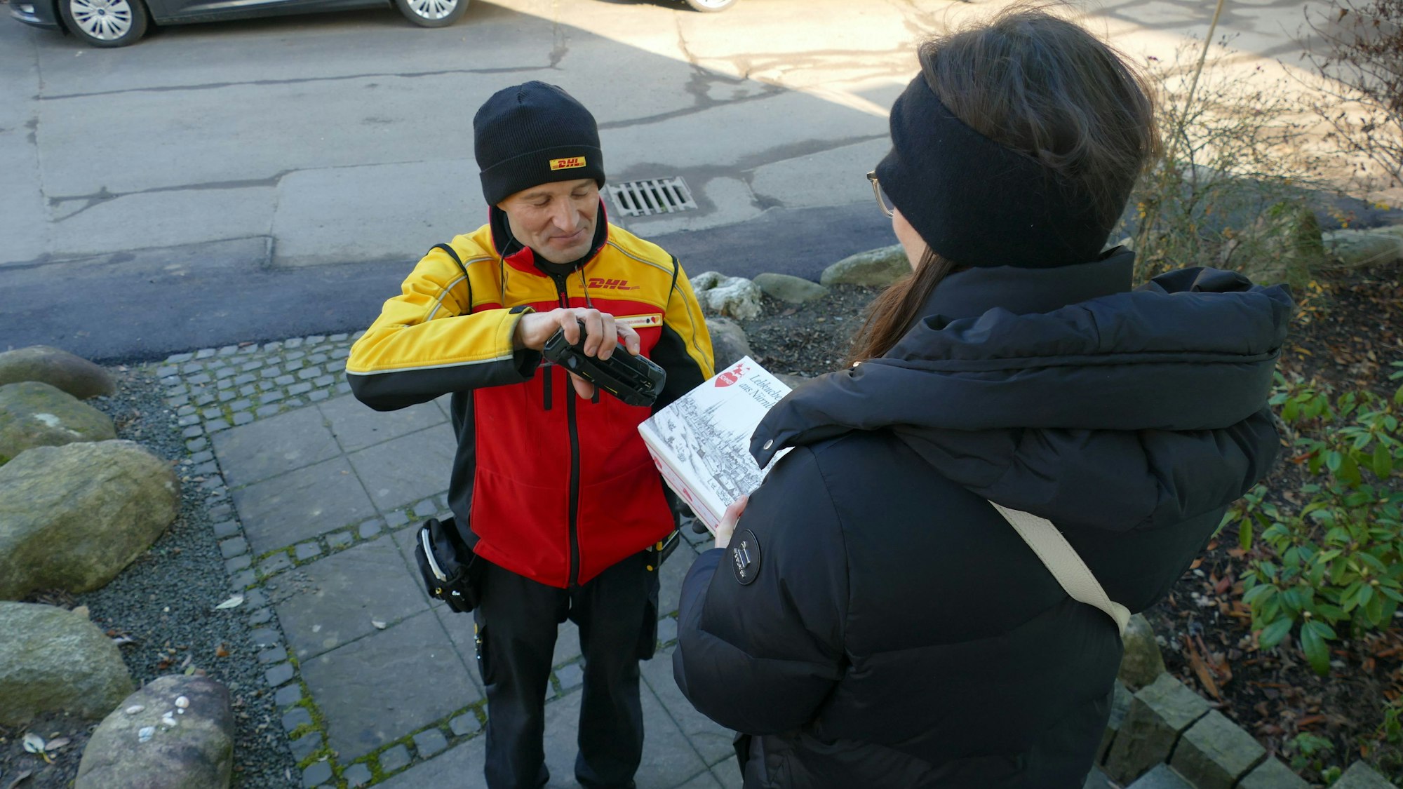 Ein Paketbote gibt ein Paket an eine Frau ab.