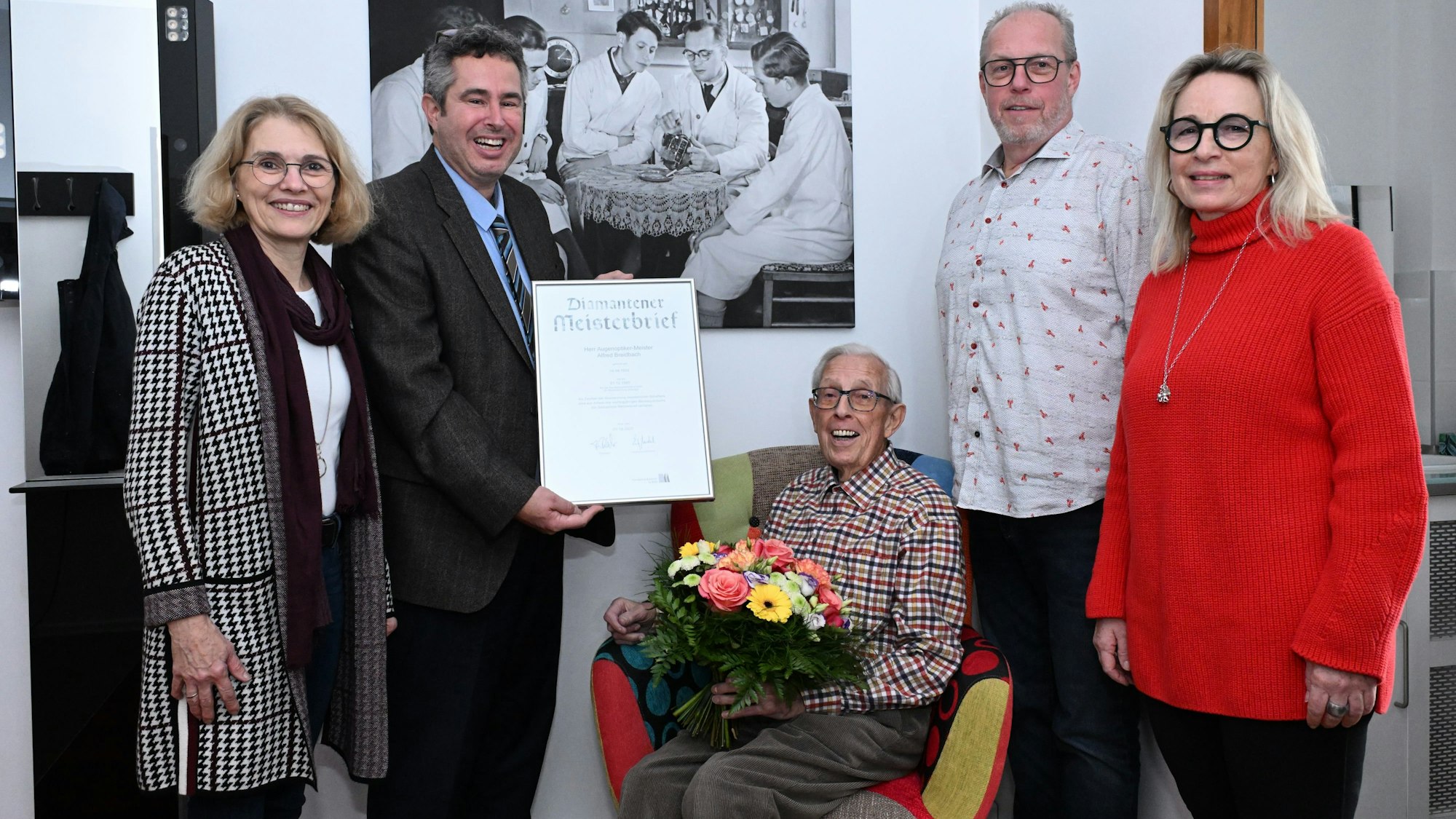 Menschen ehren einen Senior mit Blumen und einem Geschenk.