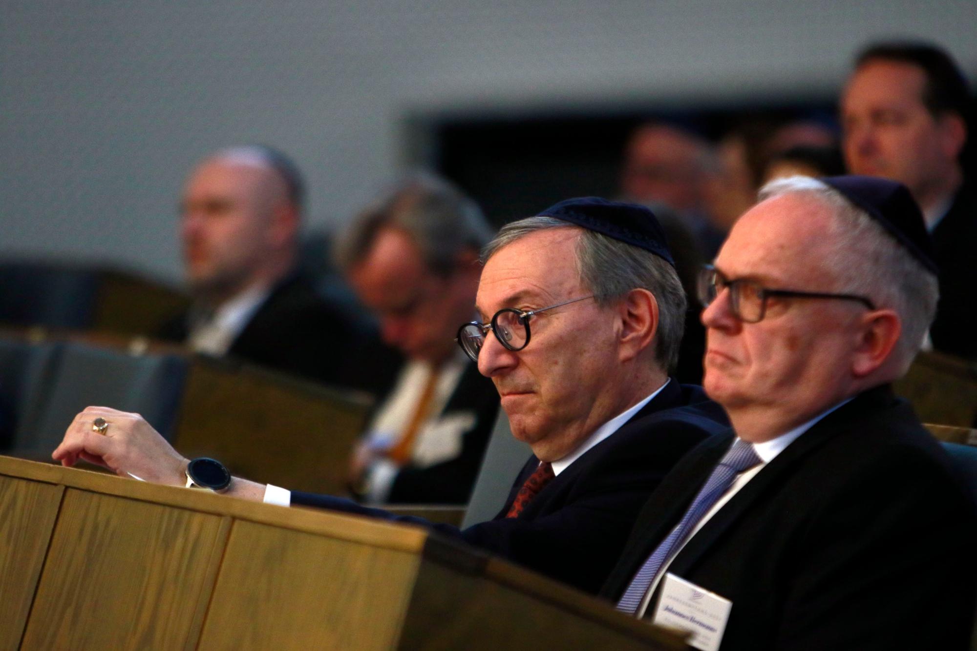Die beiden Männer sitzen in den Reihen der Synagoge. Sie tragen Anzüge.