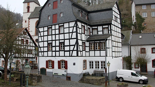 Beim Gildehaus handelt es sich um ein mehrstöckiges Fachwerkgebäude im Ortszentrum von Blankenheim. Im Hintergrund ist die Kirche zu sehen.