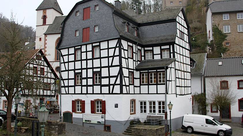 Beim Gildehaus handelt es sich um ein mehrstöckiges Fachwerkgebäude im Ortszentrum von Blankenheim. Im Hintergrund ist die Kirche zu sehen.