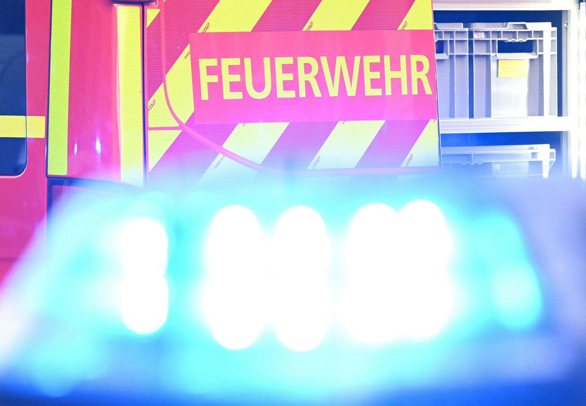 Ein Fahrzeug der Feuerwehr steht bei einem Einsatz auf einer Straße, während im Vordergrund das Blaulicht eines Polizeifahrzeugs zu sehen ist.