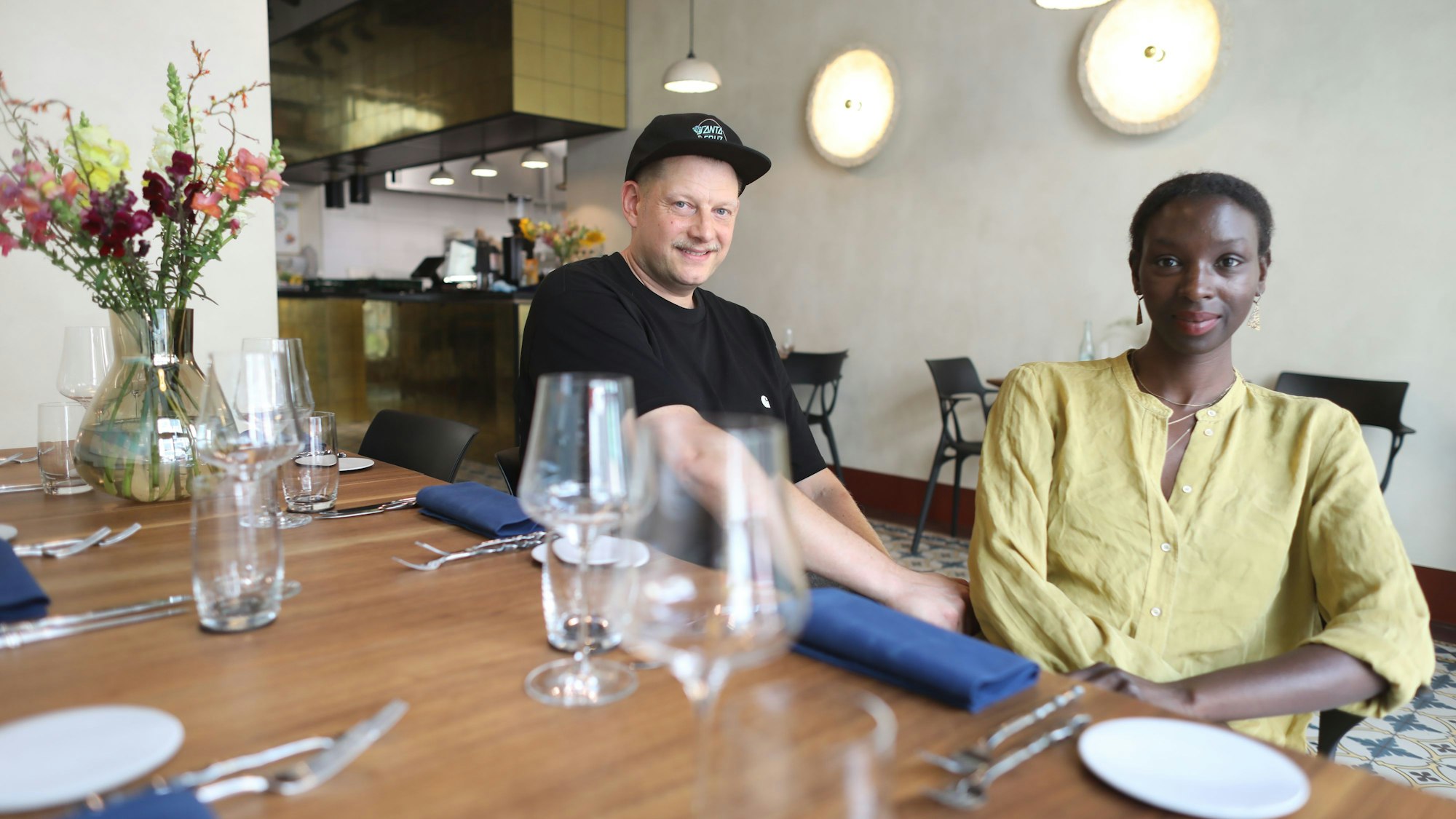 Die Restaurantbetreiber, ein Mann und eine Frau, sitzen am gedeckten Tisch.