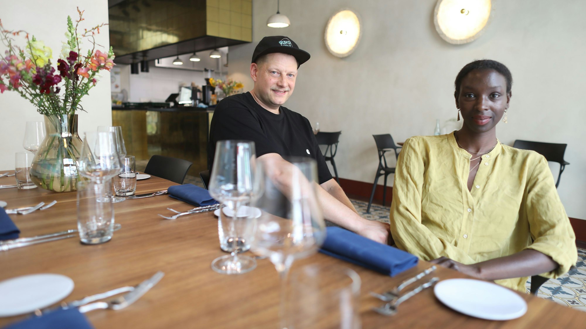 Die Restaurantbetreiber, ein Mann und eine Frau, sitzen am gedeckten Tisch.