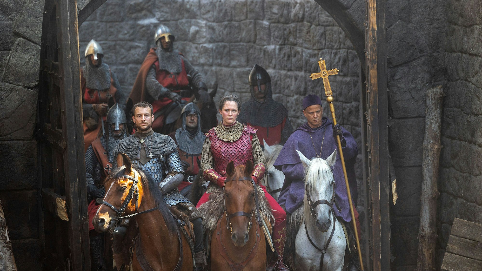 Mittelalterlich-ritterlich gekleidete Schauspieler sitzen auf Pferden. In der Mitte eine Frau, die die Königin spielt