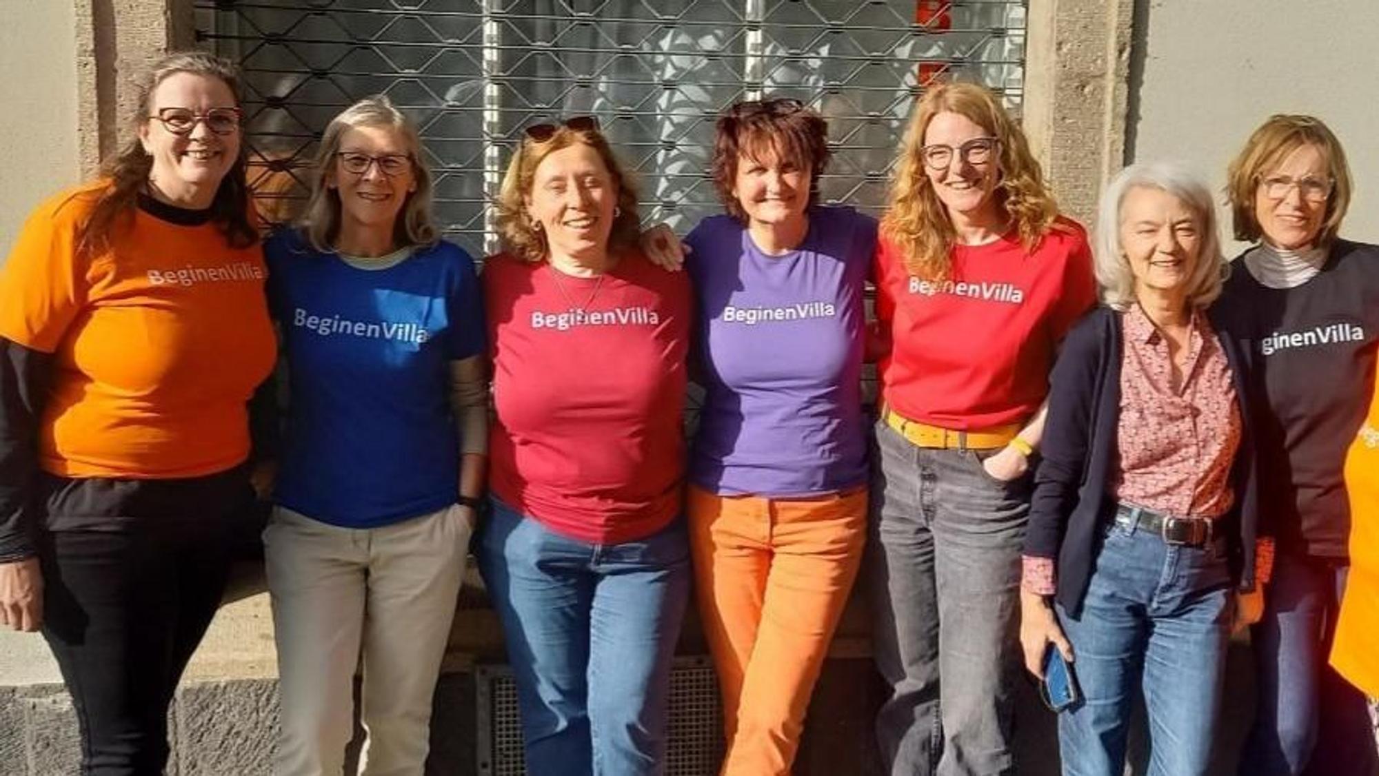 Sieben Frauen stehen Arm in Arm in bunten T-Shirts nebeneinander. Auf denen steht „BeginenVilla“.