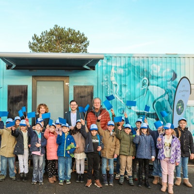 Viele Kinder winken mit blauen Fähnchen, dahinter stehen drei Erwachsene.