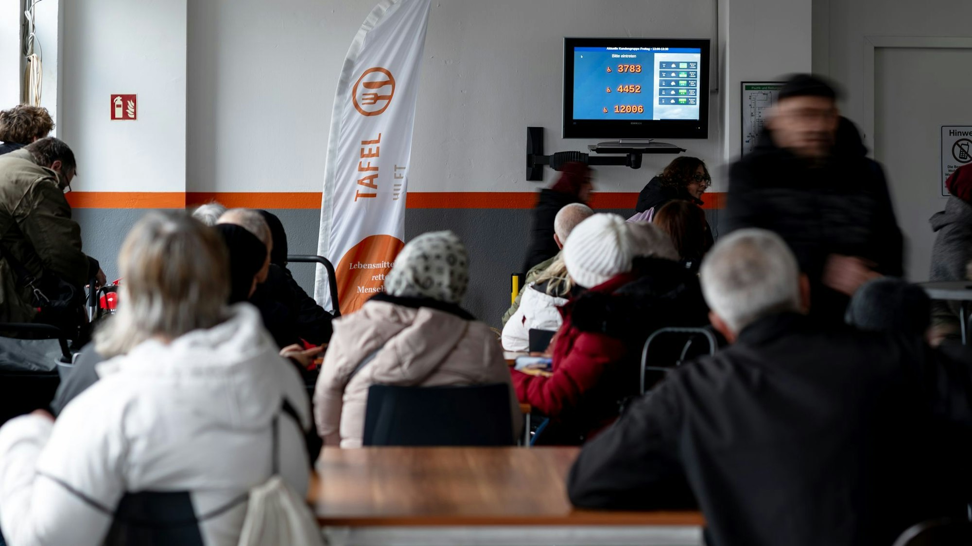 Tafelkunden warten an der Lebensmittelausgabe, bis ihre Nummer an der Reihe ist - Schlangestehen ist in vielen NRW-Tafeln nicht mehr notwendig.