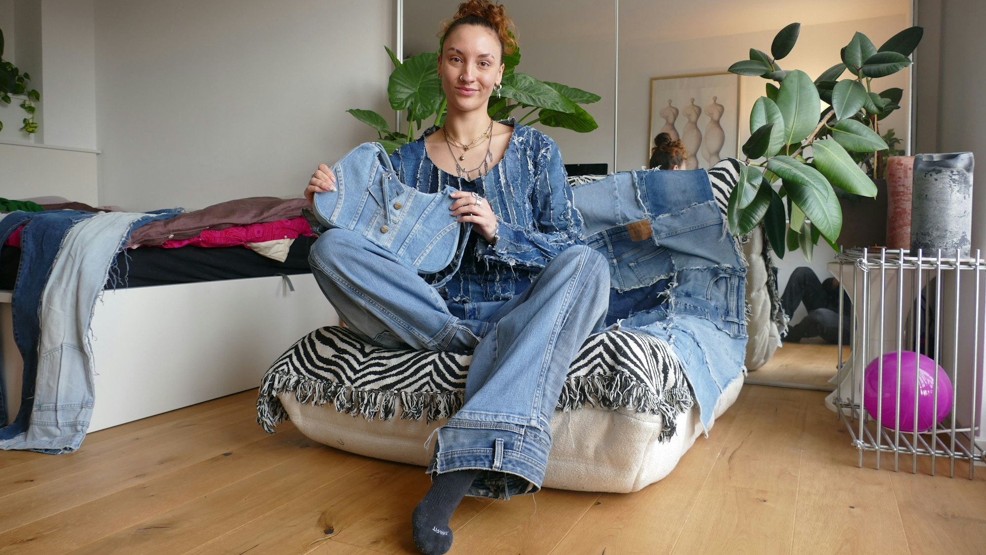 Eine junge Frau sitzt auf einem Sessel. Sie hält eine Tasche aus Jeans-Stoff in der Hand.