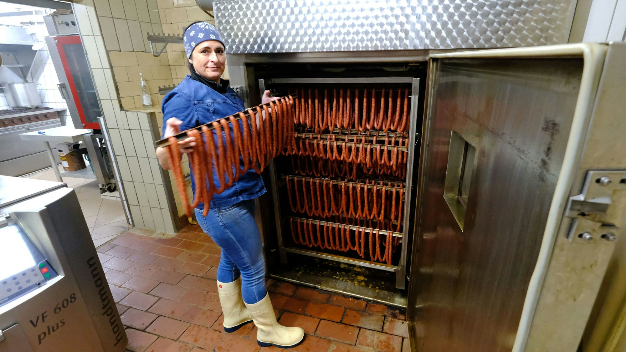 Die Mitarbeiterin einer Metzgerei holt frische Mettwürstchen aus dem Räucherofen.