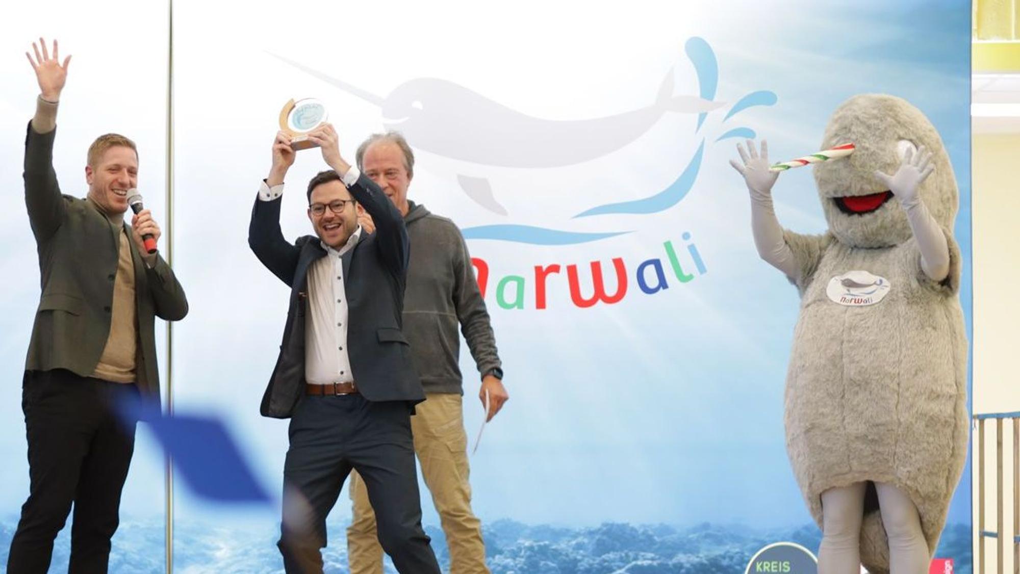Markus Ramers übergibt Emmanuel Kunz den „Narwali-Pokal“. Rechts im Bild ist das Maskottchen Narwali zu sehen.