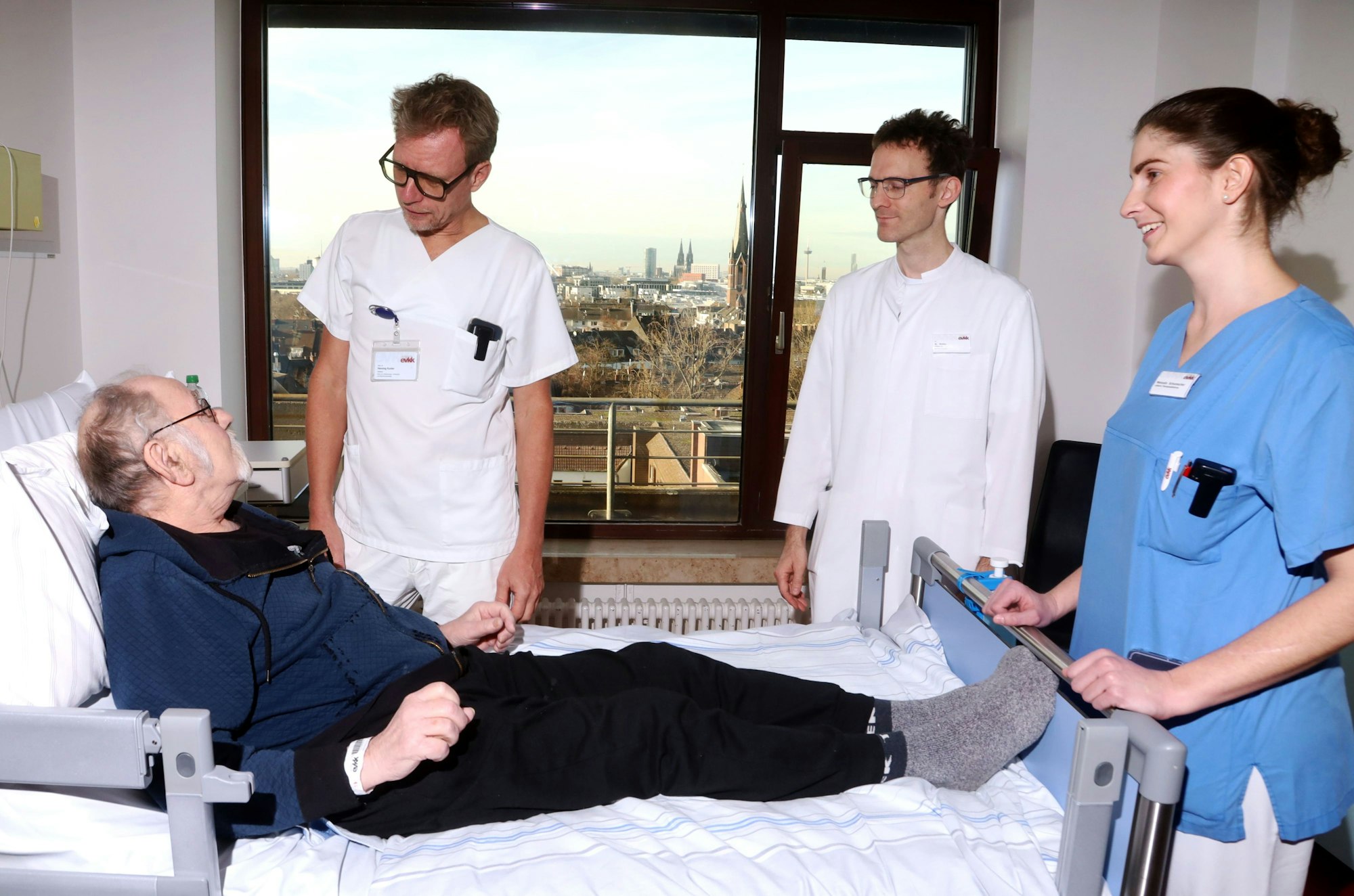 16.12.2024, Köln: Stürze im Alter verhindern. Wie kann das gelingen? Ein Besuch im Evangelisches Krankenhaus Kalk. Chefarzt Henning Kunter, Oberarzt Wolf Wallis (v.l.) und Thearpeutin Manuela Schumacher bei Guido Lau. Foto: Arton Krasniqi