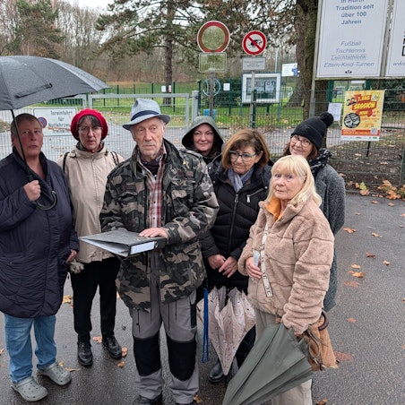 Das Foto zeigt eine Gruppe von Menschen mit einem Aktenordner vor dem Sportplatz in Efferen.