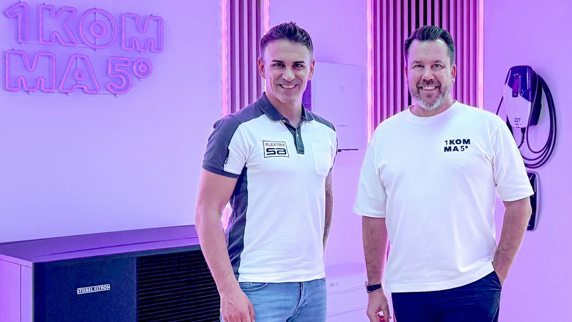 Das Bild zeigt die beiden Obengenannten, die in einem Verkaufsraum stehen und in die Kamera lächeln.