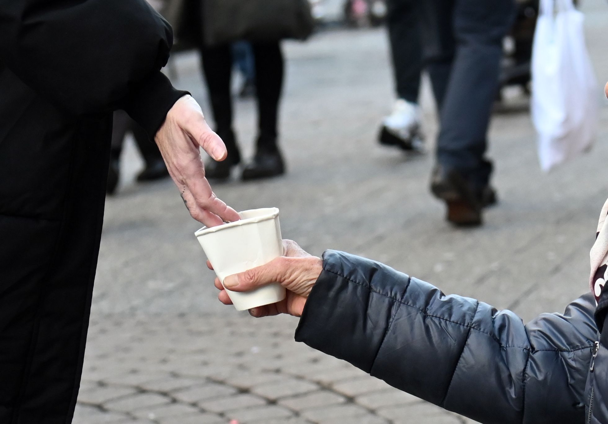 Eine Frau bittet mit einem Pappbecher um Spenden.