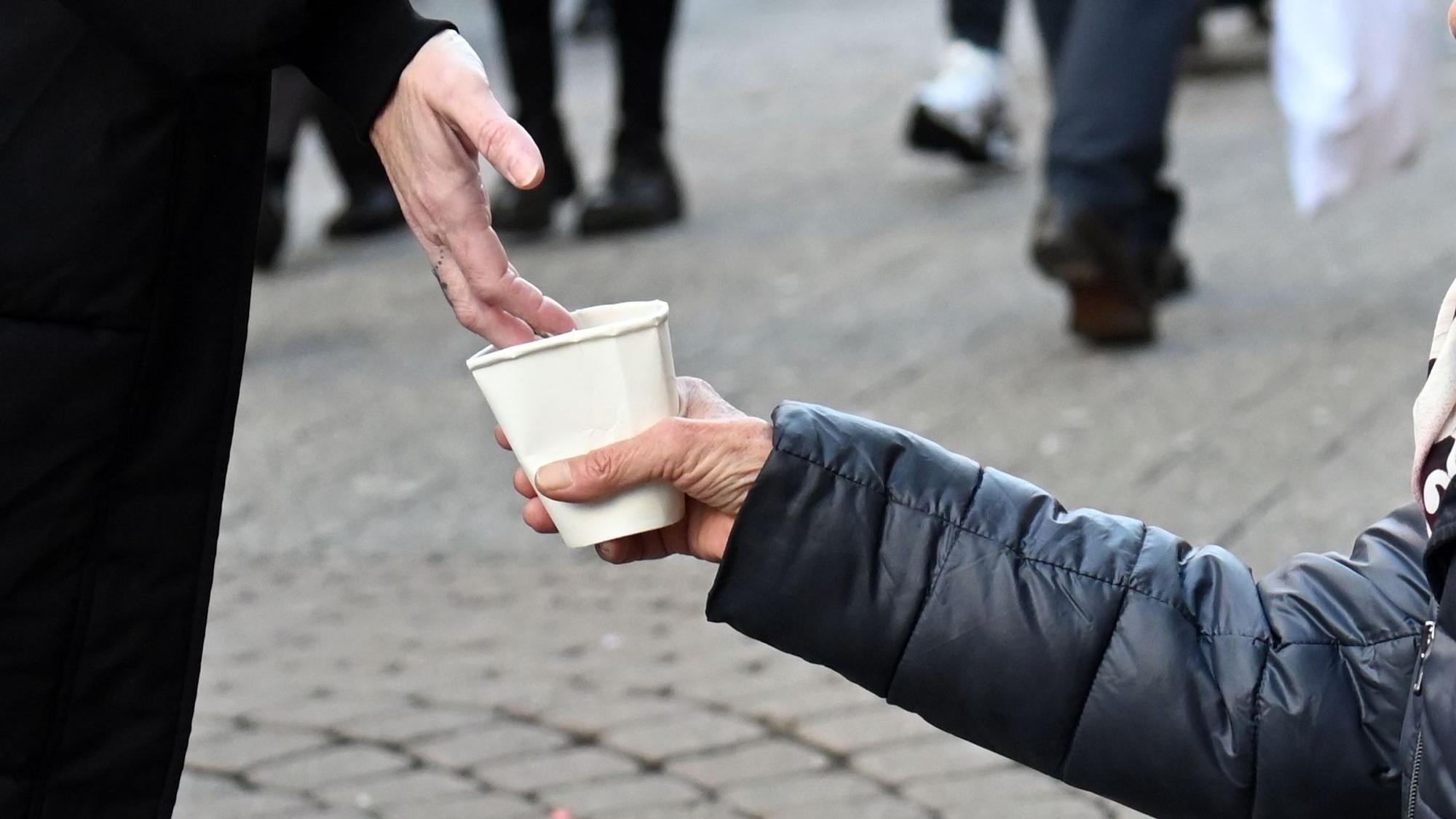 Eine Frau bittet mit einem Pappbecher um Spenden.