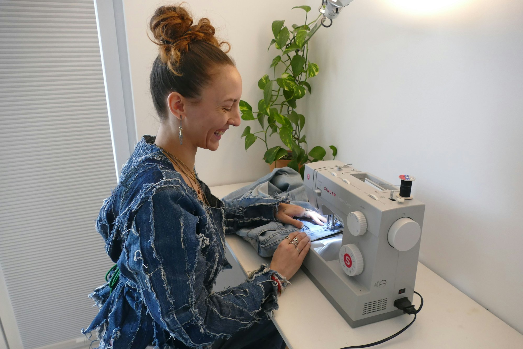 Eine junge Frau, die ein fransiges Jeansoberteil trägt, sitzt an einer Nähmaschine.