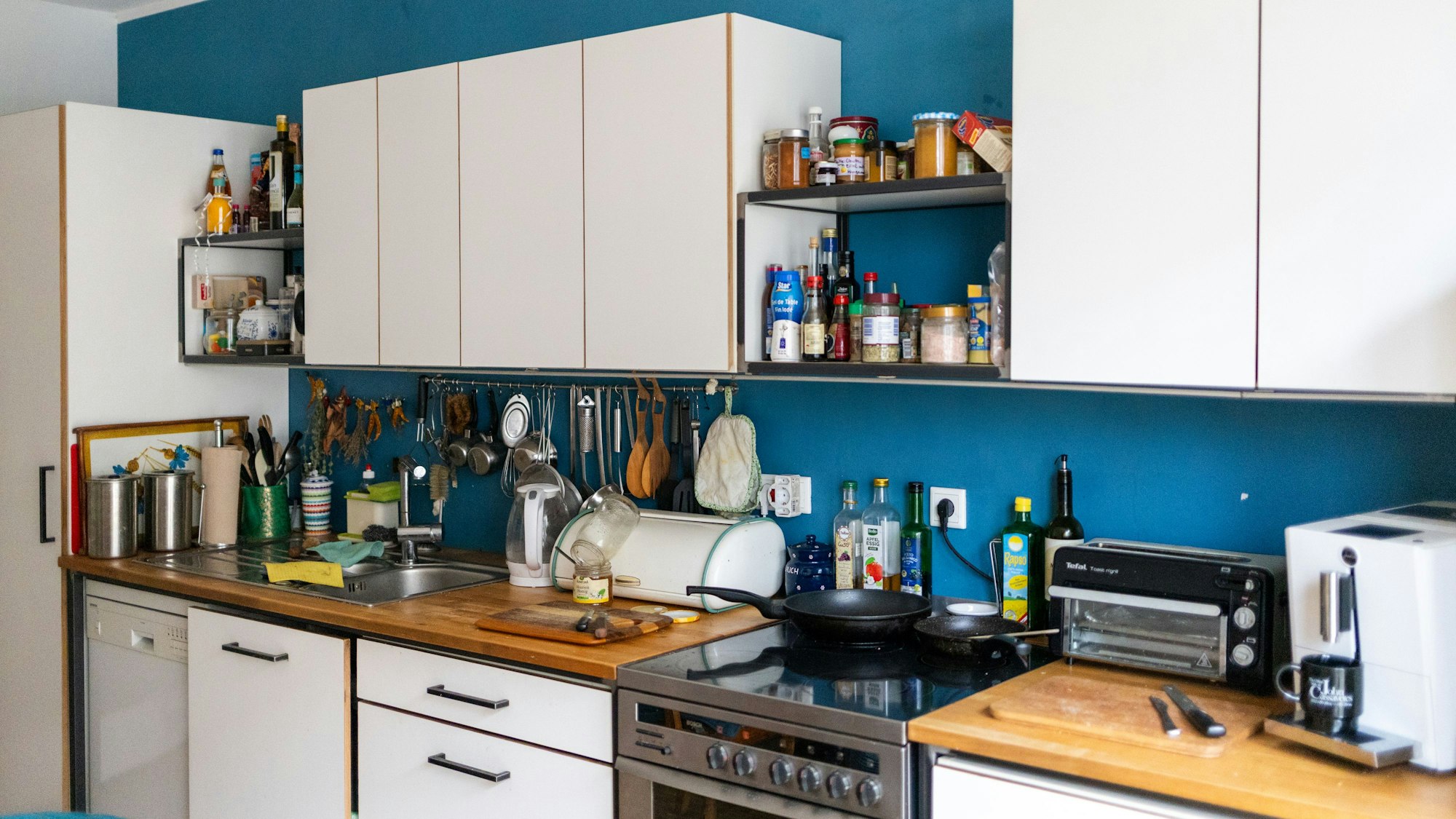 Der Blick in eine Küche. Auf dem Herd stehen Pfannen, Gewürze im Regal.