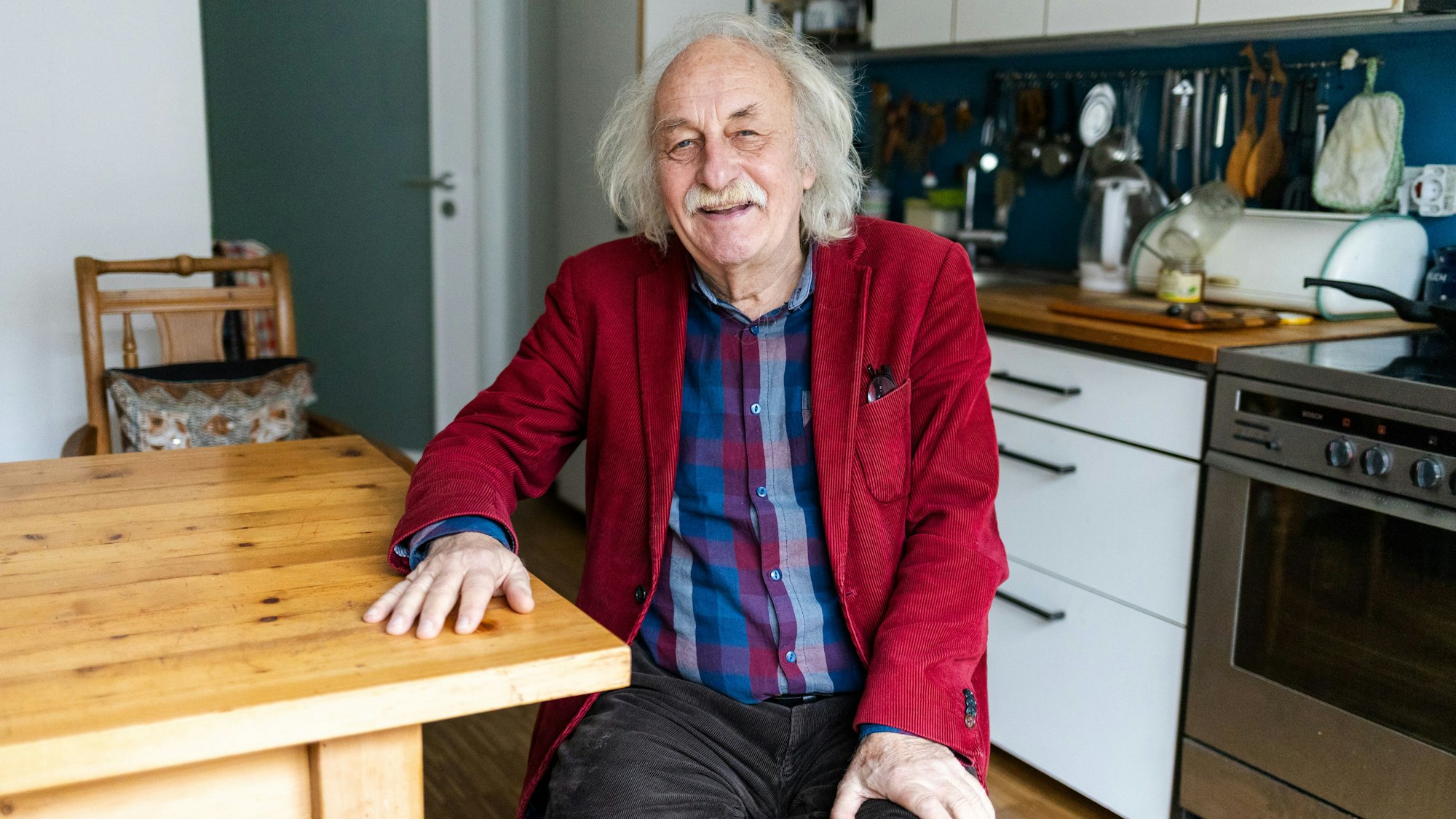 Ein Mann sitzt in einer Küche und lacht in die Kamera.