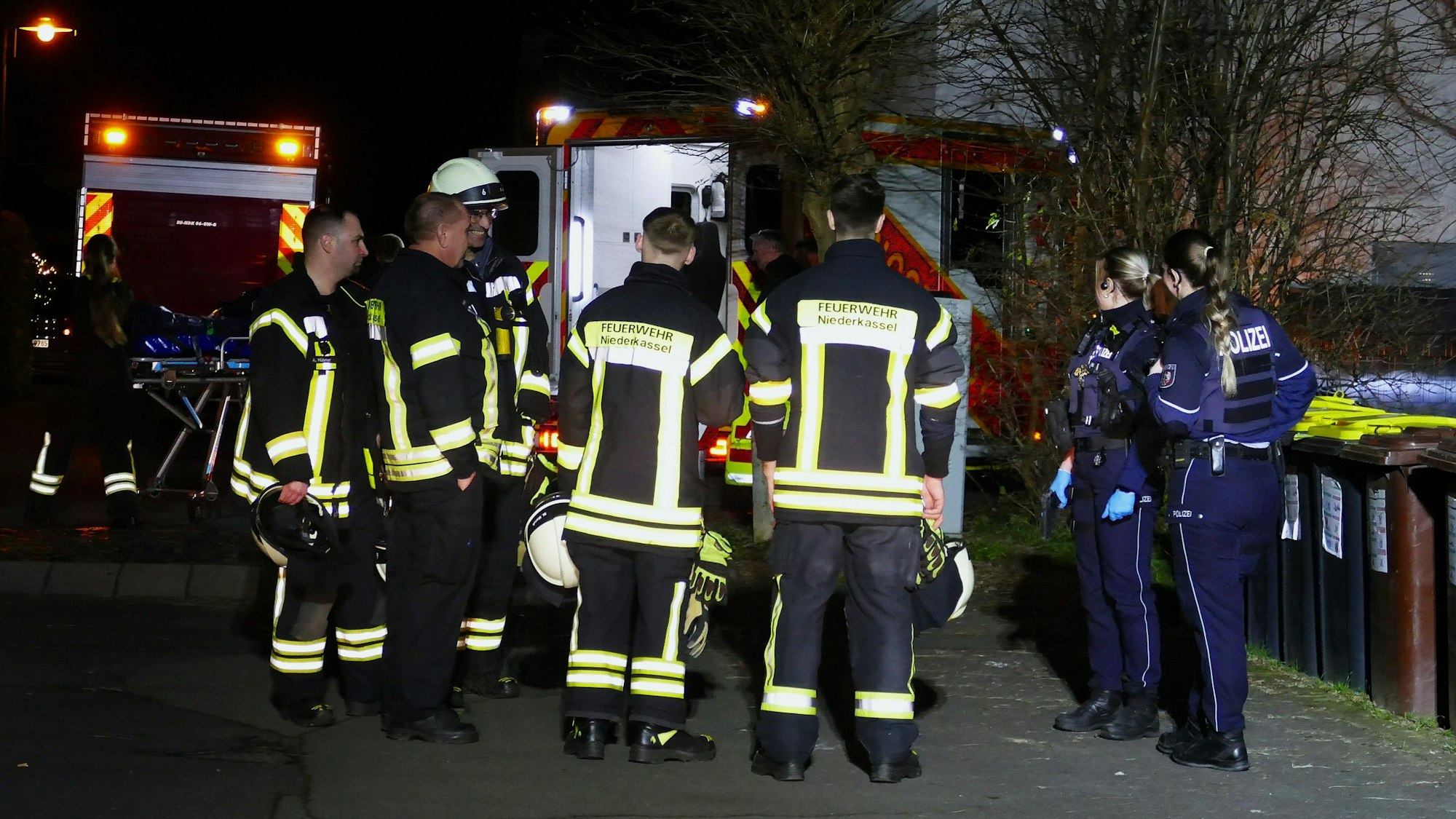 Einsatzkräfte von Feuerwehr und Polizei stehen in der Dunkelheit auf einer Straße.