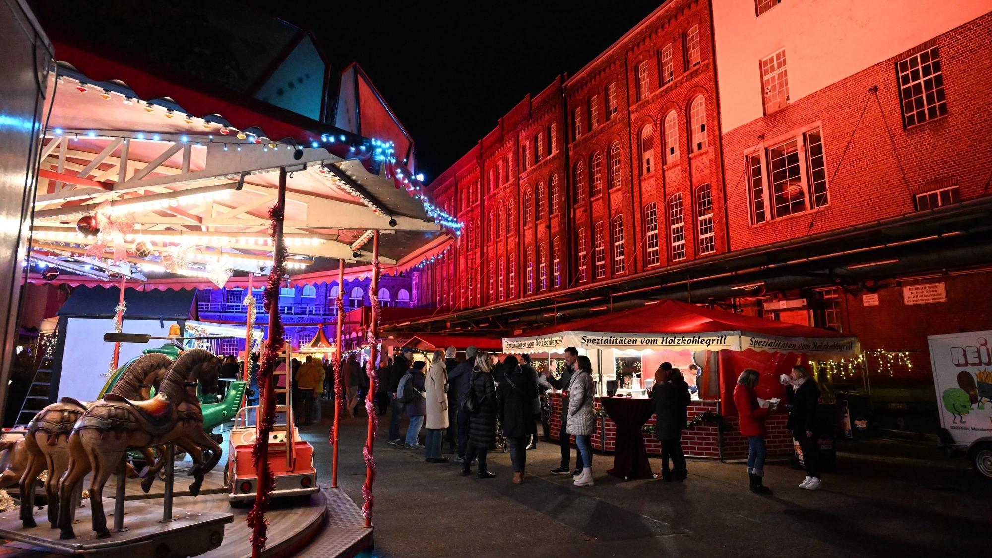 Zu sehen ist ein Kinderkarussell vor einem rot angeleuchteten Backsteingebäude.