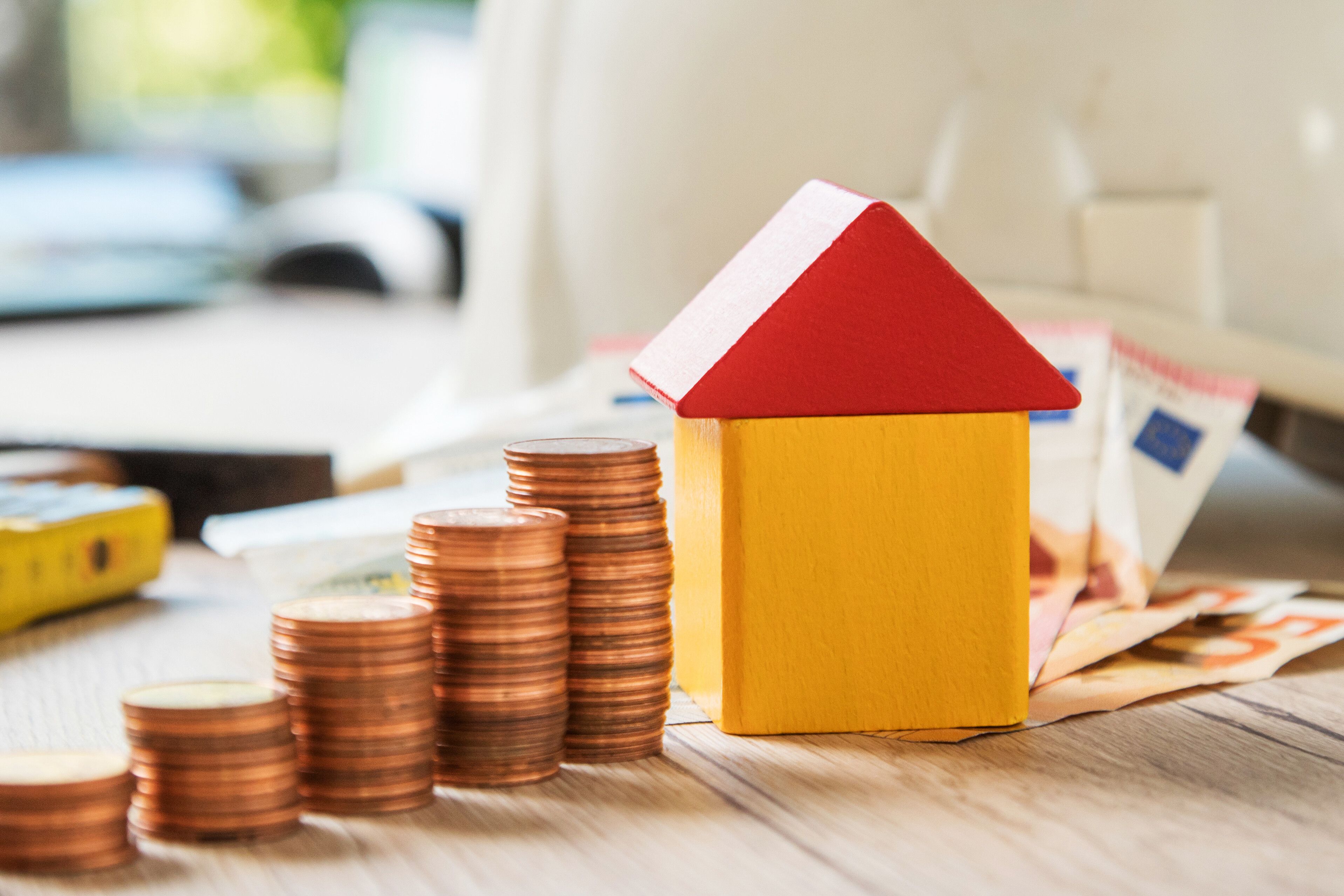 Zusehen sind ein Miniaturhaus und Münzen sowie Scheingeld