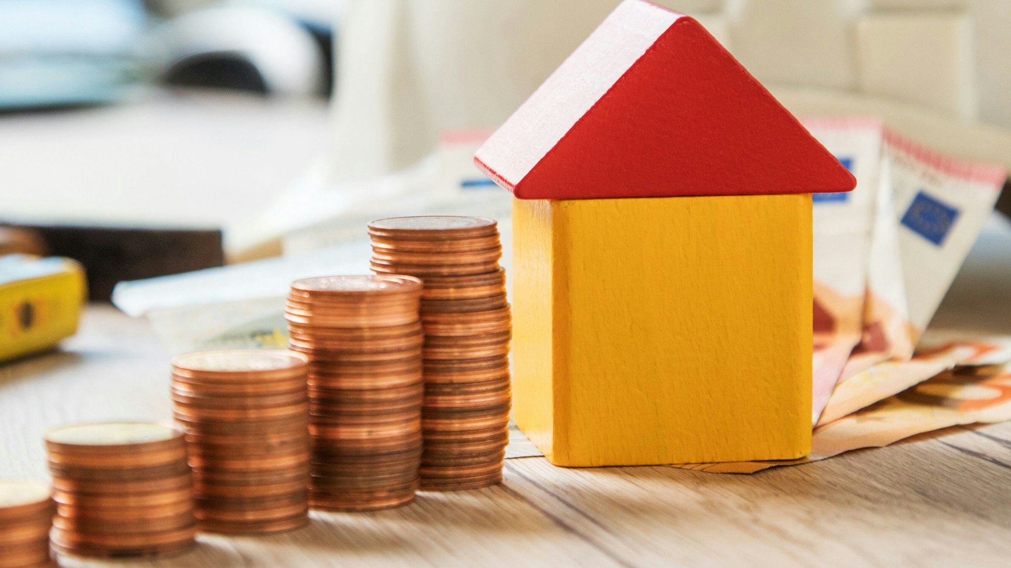 Zusehen sind ein Miniaturhaus und Münzen sowie Scheingeld