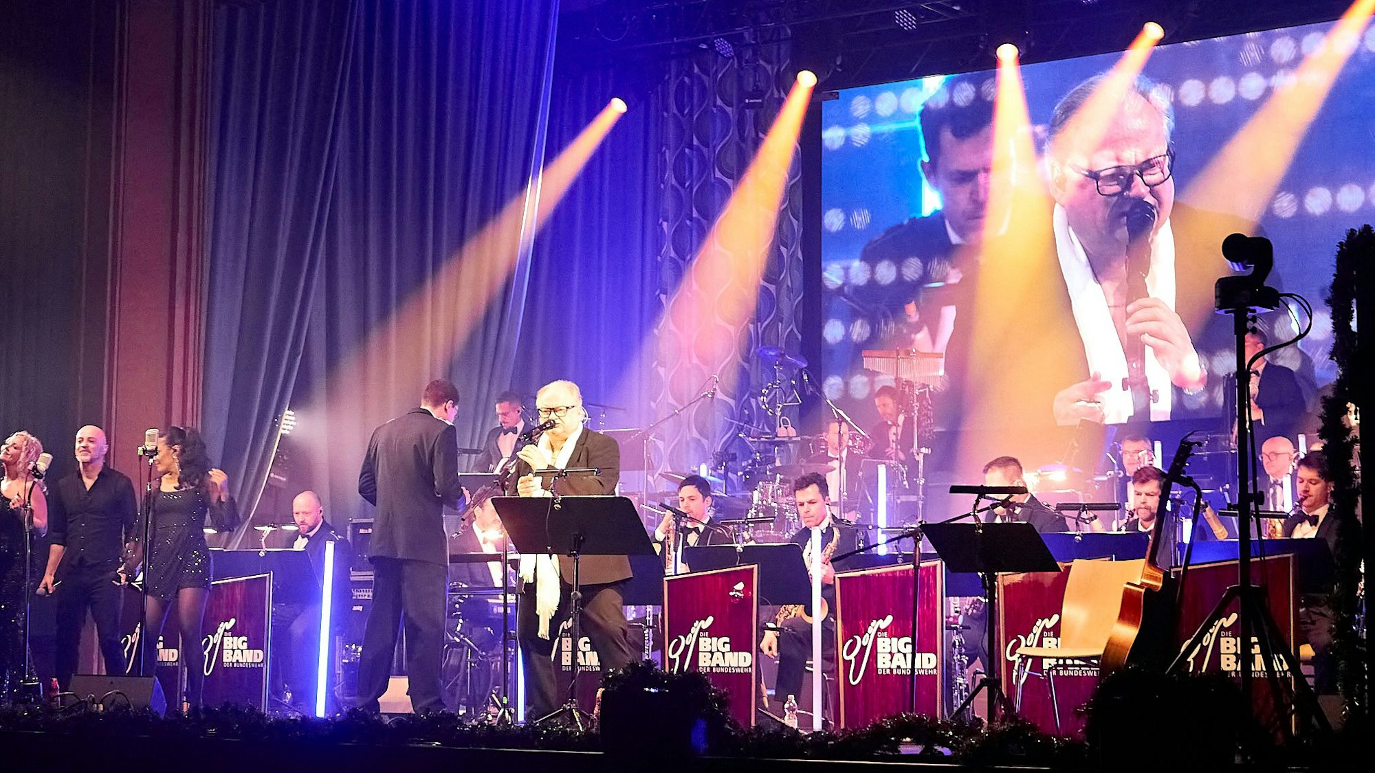 Auf einer mit Strahlern erleuchteten Bühne musizieren Heinz Rudolf Kunze und die Bigband der Bundeswehr.