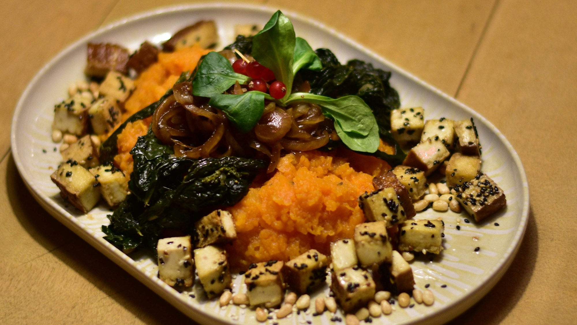 Gebratener Sesam-Tofu auf Süßkartoffelstampf und italienischem Palmkohl mit geschmolzenen Zwiebeln und Pinienkernen.