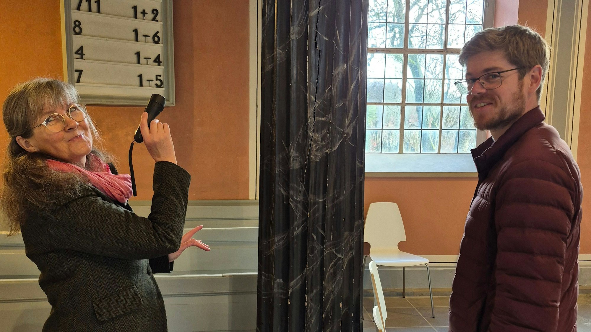 Architektin Susanne Schneider-Jacobs und Küster Tim Becker schauen sich die Schwundrisse der Säulen in der Kirche aus der Nähe an.