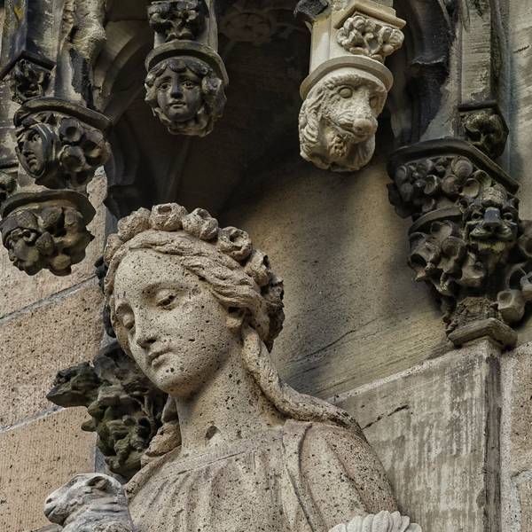 Eine Hundekopf-Skulptur an einem Stein-Baldachin über der Statue einer Frau. An dem Baldachin hänge auch andere Gesichter.