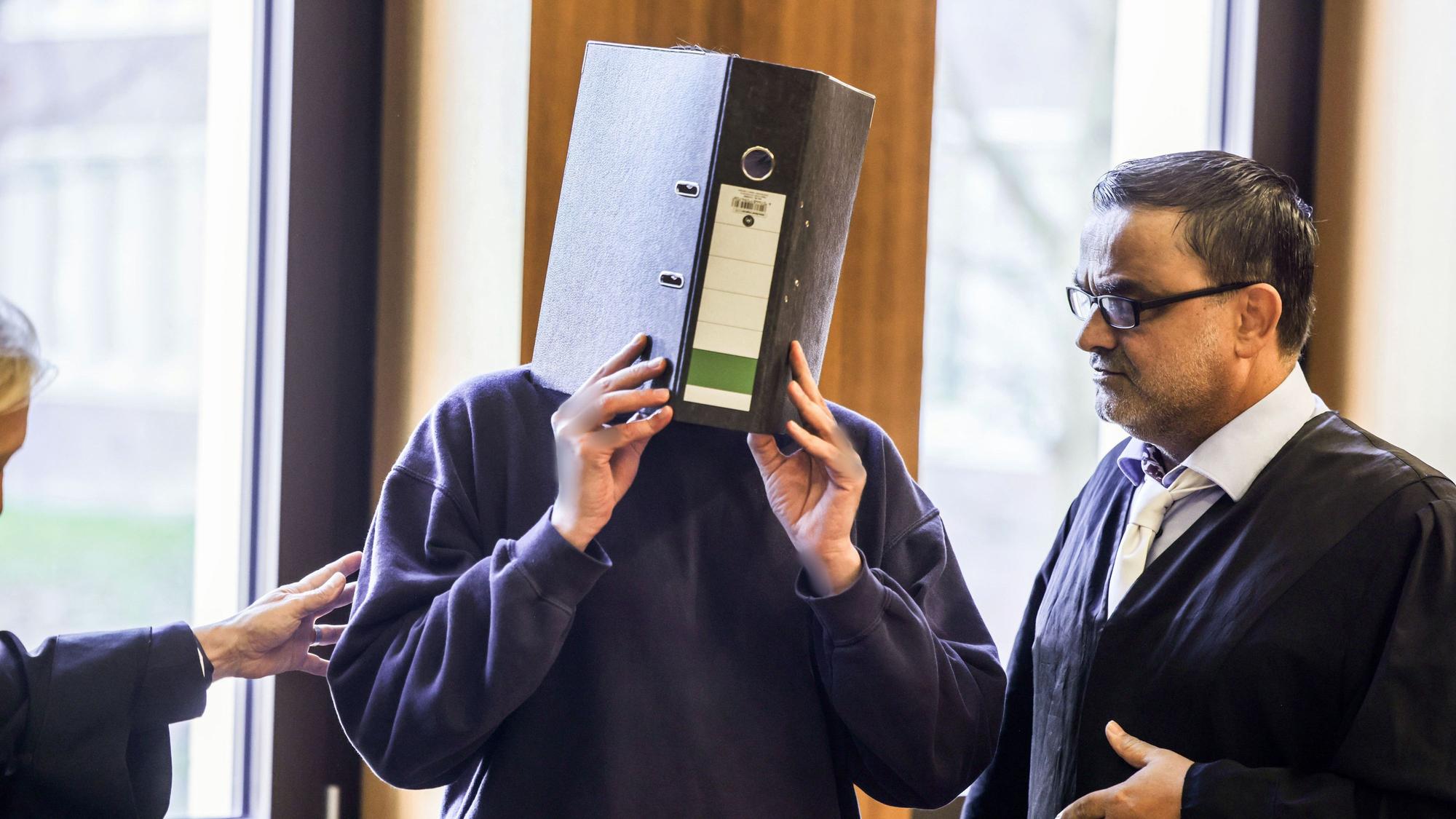 Der Angeklagte Krankenpfleger (M) steht mit einem Aktenordner vor dem Gesicht neben seinem Anwalt Volker Breyer (r) im Gerichtssaal. Das Aachener Landgericht hat Ulrich S. vor einem Monat wegen des Mordes an zehn Patienten zu einer lebenslangen Freiheitsstrafe verurteilt.