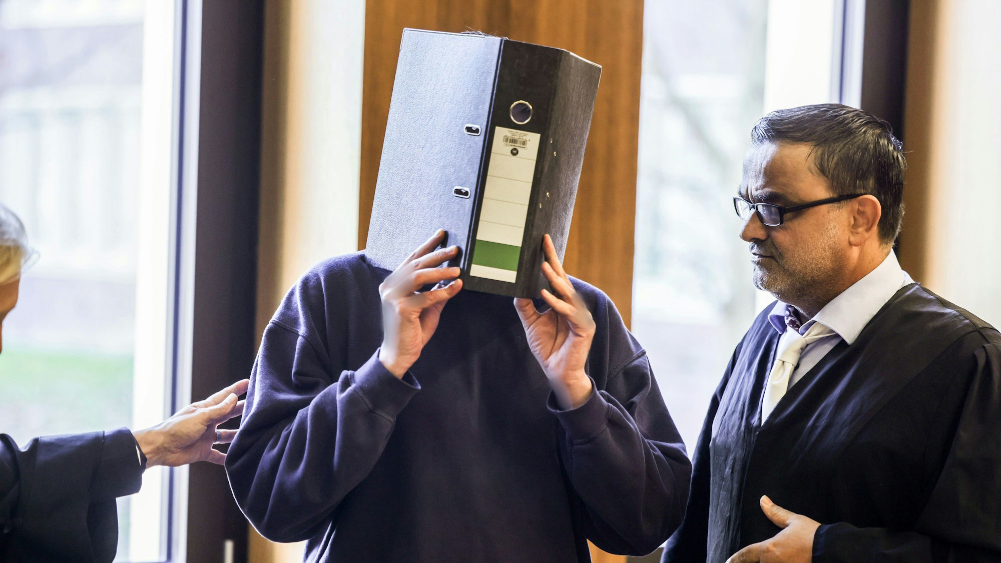 Der Angeklagte Krankenpfleger (M) steht mit einem Aktenordner vor dem Gesicht neben seinem Anwalt Volker Breyer (r) im Gerichtssaal. Das Aachener Landgericht hat Ulrich S. vor einem Monat wegen des Mordes an zehn Patienten zu einer lebenslangen Freiheitsstrafe verurteilt.