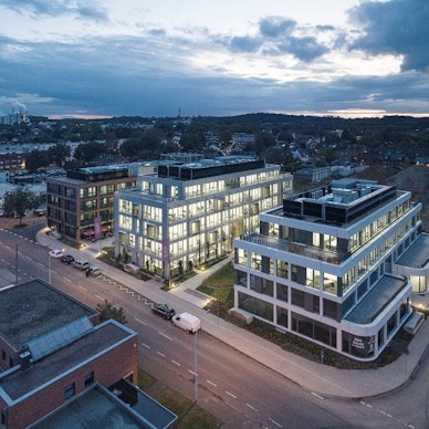 Auf dem Bild ist eine Luftaufnahme von drei erleuchteten Bürogebäuden zu sehen.