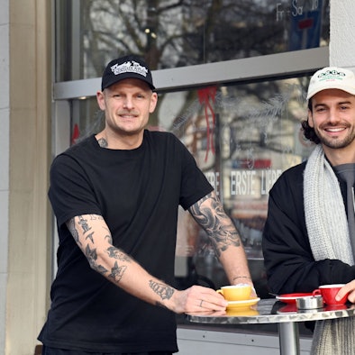 Chris Schneider und Tim Stutzenstein stehen an einem Stehtisch und trinken Kaffee.