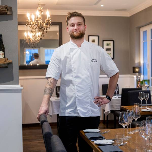 Ein junger Mann steht in weißem Koch-Hemd in seinem Restaurant.