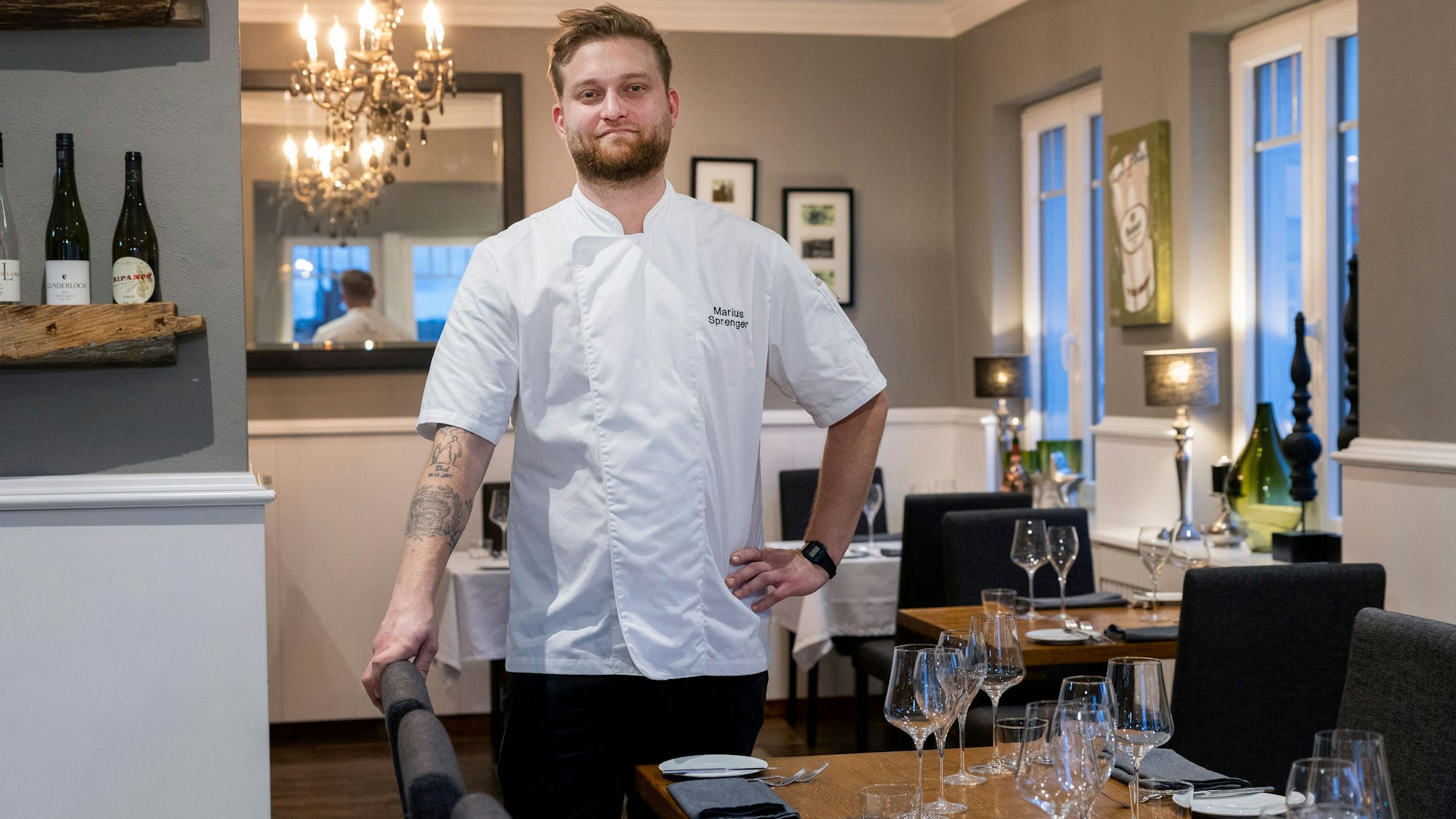 Ein junger Mann steht in weißem Koch-Hemd in seinem Restaurant.